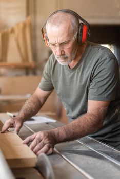 Adult man with safety glasses cutting wood on a sliding table saw, upright