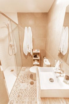 A small and cozy beige tiled bathroom with shower, toilet and sink with mirror from a hotel. Concept of hotel, lodging.