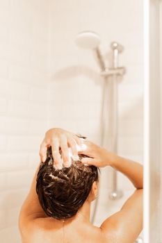 Vertical image of a woman on her back taking a shower while soaping her hair with shampoo in a hotel.