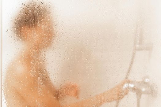 View through the glass of a shower cabin of an unrecognizable caucasian woman taking a shower in a hotel with copy space.