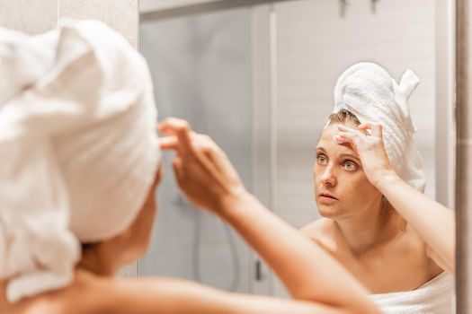 Adult woman applying moisturizing skin care cream on forehead after shower at a hotel. Concept of skin care.