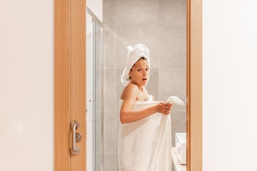 Surprised adult woman caught unawares in bathroom after taking a shower. Concept of hotel.