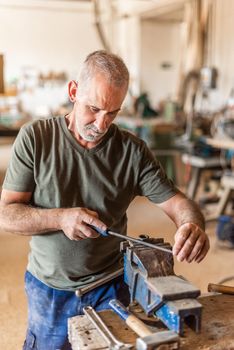 Male worker filing a metal tool over a workbench, vertical picture