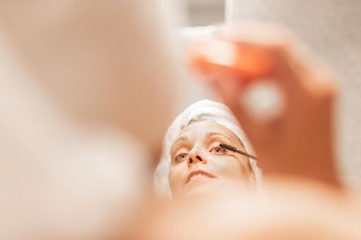 Adult woman applying mascara on eyelash in bathroom of a hotel while looking in the mirror. Concept of beauty.