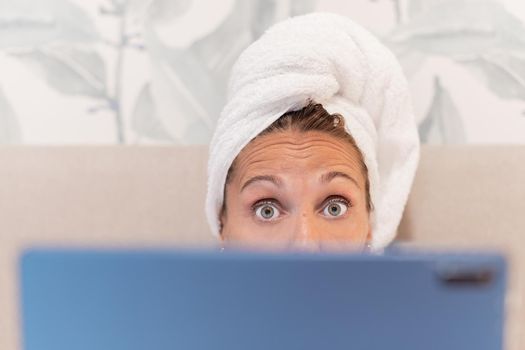 Close up of a woman wrapped in towels looking at camera while using her digital tablet on bed of a hotel room. Concept of vacation, hotel.