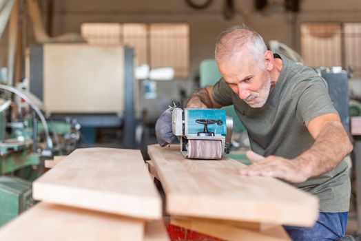 Focused male person working with a hand sander checking the plank, horizontal background