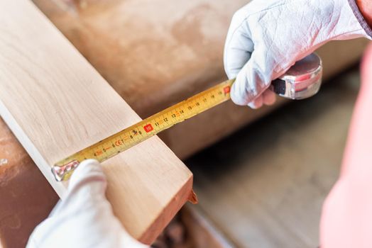 Person measuring a wooden plank with a meter, horizontal view