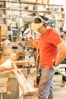 Adult man with a face shield and an iron cutter, working with wood, vertical