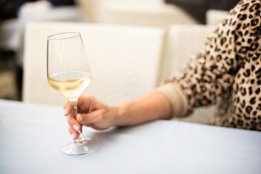 Selective focus on a glass of white wine in the hand of a caucasian woman sitting in a restaurant