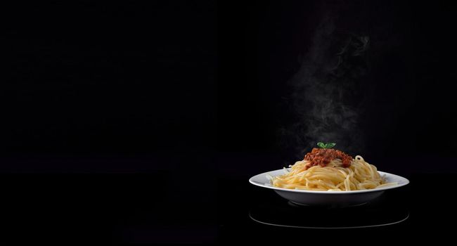 Steaming delicious spaghetti bolognese on black background. Empty text space