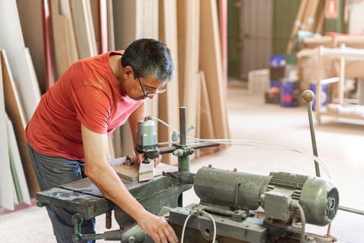 Male adult with glasses and red t-shirt drilling wood in a manufacturer plant