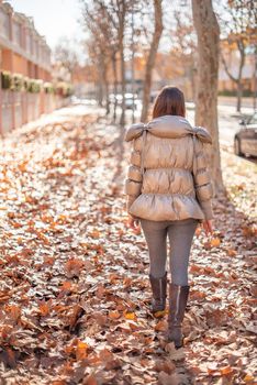 Vertical photo of a caucasian woman with winter clothes walking in the street full of fallen leaves