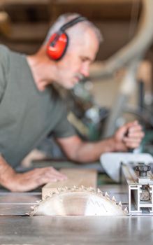 unfocused male person cutting timber on a sliding table saw, vertical