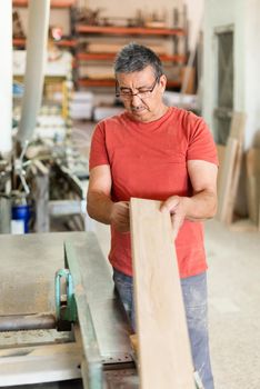 Adult man with red t-shirt reviewing a wooden plank, vertical, unfocused background