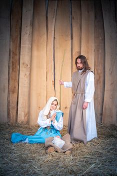 Vertical photo of nativity with the virgin mary seated next to baby jesus and Joseph standing in a crib