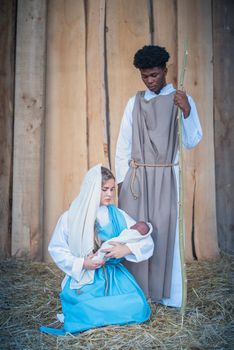 Vertical photo of caucasian virgin mary holding a baby next to a black Joseph character in a crib