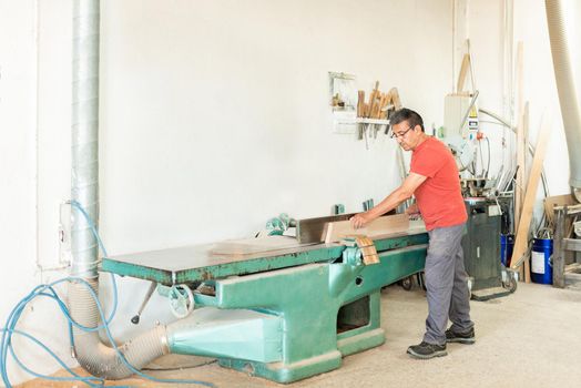 Adult male working manually with a wood planing machine, horizontal view