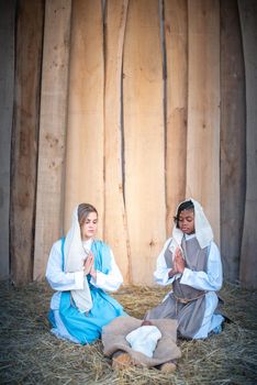 Vertical photo of lgtb nativity scene with two virgin marys praying next to an african Jesus baby