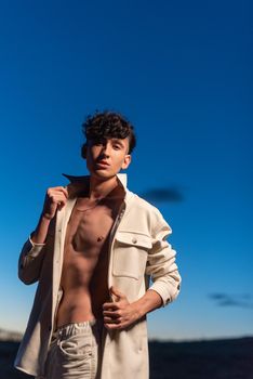Vertical portrait of a non binary caucasian fit person posing with a jacket during sunset