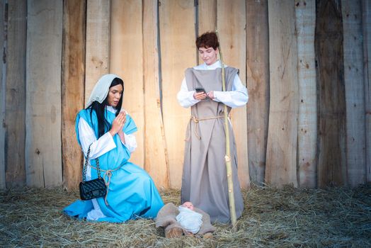Nativity scene with transgender people using a mobile phone and carrying a handbag in a crib