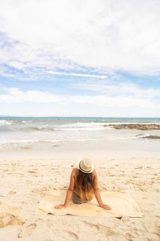 Vertical photo of a woman with hat lying on the white sand of a beach in front of the sea. Formentera in Spain