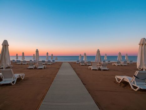 Umbrellas and sun loungers on the calm sea beach at sunrise