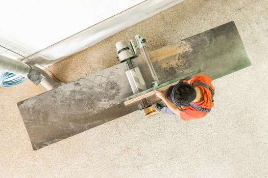 Top view of anonymous male carpenter in uniform trimming wooden plank on professional woodworking planer while working in light carpentry