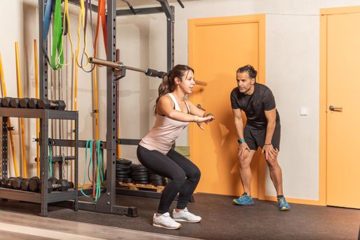 Sportswoman doing squats without weighting exercise with trainer in gym. Concept of gym.