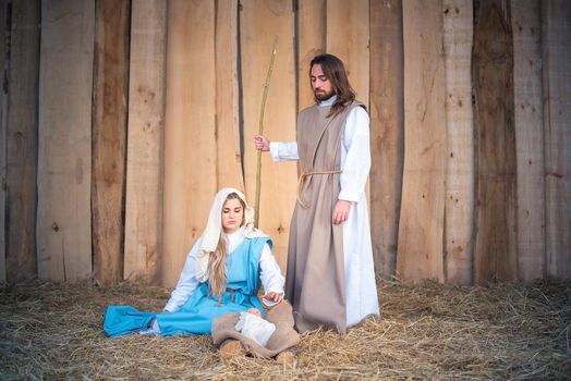 Traditional nativity with the virgin mary seated next to baby jesus and Joseph standing in a crib