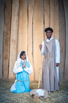 Vertical portrait of black virgin mary and black joseph praying next to jesus baby in a crib