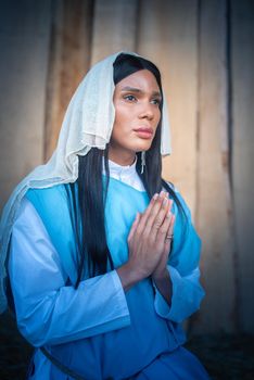 Vertical portrait of a transsexual virgin praying with her gaze lost in a nativity scene