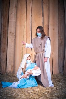 Vertical photo of a nativity scene with the characters wearing masks while she holds Jesus baby