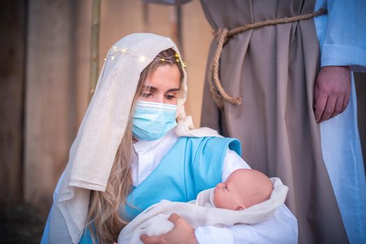 Caucasian woman with mask representing virgin mary holding Jesus baby in a nativity scene