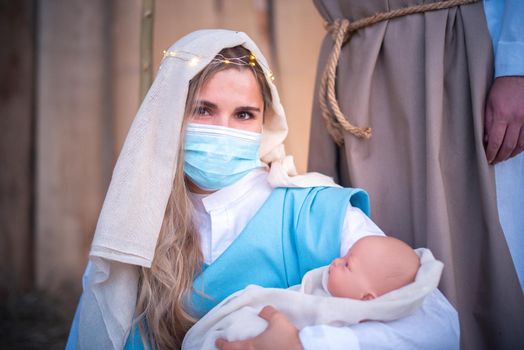 Caucasian woman with mask representing virgin mary facing the camera while holding a baby in a crib