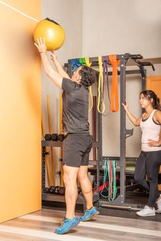 Sportsman doing medicine ball throw exercise in gym while sportswoman look at him. Concept of exercise with equipment in gym.