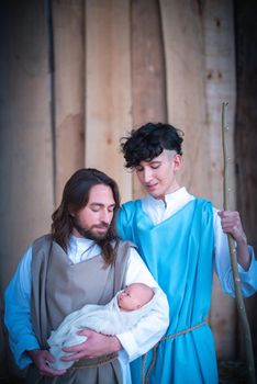 Vertical portrait of two men representing virgin mary and joseph in a nativity scene holding a baby