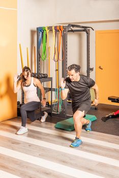 Front side view of athlete woman and man doing lunges exercises for leg muscle workout training in gym. Concept of exercises in gym.