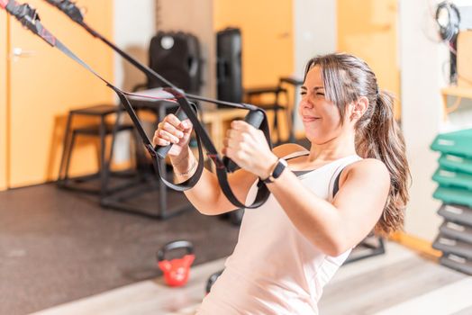 Sportswoman doing exercise with expression of suffering with trx fitness straps at gym. Concept of trx training.