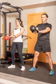 Sportswoman and man doing kettlebell swing exercise at gym. Concept of exercises with equipment in gym.