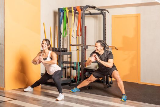 Cheerful people doing adductor stretch exercise in gym, woman looking at camera. Concept of exercise in gym.