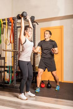 Woman doing shoulder exercise with dumbbells in the gym. Concept of exercise with equipment at gym.