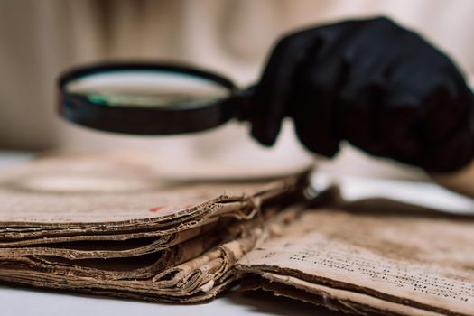 Historian scientist in gloves reading antique book with magnifying glass. Translation of religious literature. Manuscript with ancient writings. Treasures of the past. Museum piece. High quality