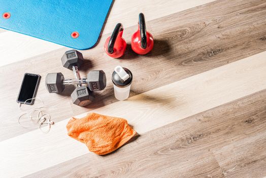 Top view of Kettlebells, foar roller, dumbbells, a bottle of water, a towel and a cell phone with headphones connected against a wooden background. Concept of equipment of gym and personal stuff.