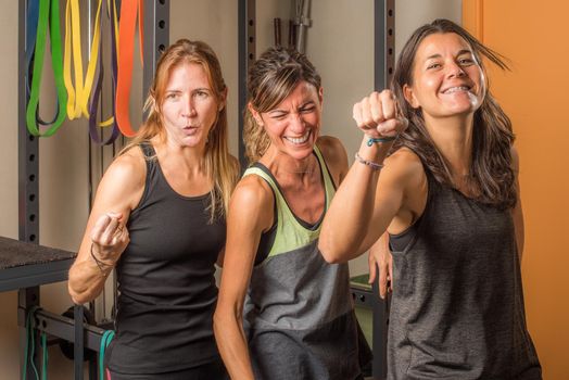 Portrait of three sportswoman showing closed fists in funny way in gym. Concept of people in gym.