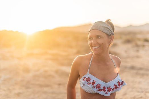 Portrait of happy smiling female tourist in swimwear and headband looking away against sunset during vacation on beach in Almeria Andalusia Spain