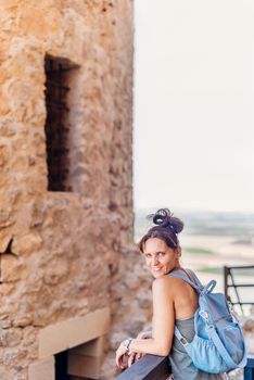 Vertical photo of a woman looking at the camera while leaning on a railing next to historic castle in Toledo, Spain.