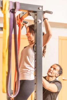 Cropped view of a sportswoman doing pull ups exercise with bar with help of trainer in gym. Concept of exercise with equipment in gym.