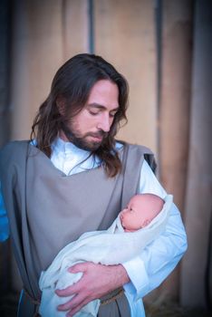 Vertical portrait of a gay representation of the nativity where joseph holding jesus baby in a crib