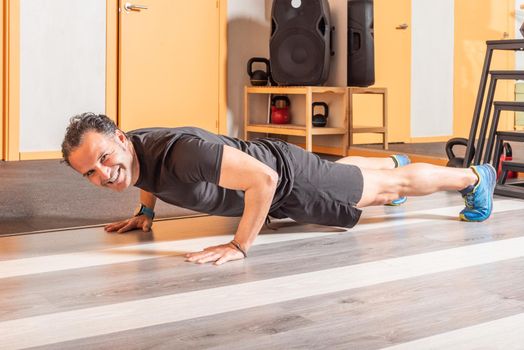 Sportsman looking at camera with smile doing push ups in health club. Concept of exercises in health club.