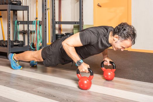 Athlete man doing push ups excercise with kettlebells in gym. Concept of exercise with equipment in gym.